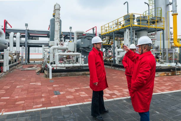 "Engineers inspecting an industrial gas processing facility in red protective coats and white hard hats"