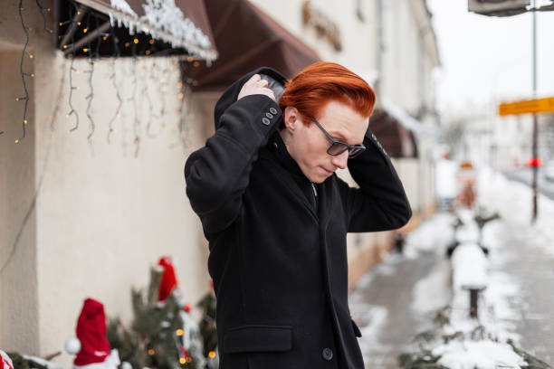 Young person with red hair wearing a black hoodie in a winter urban setting.