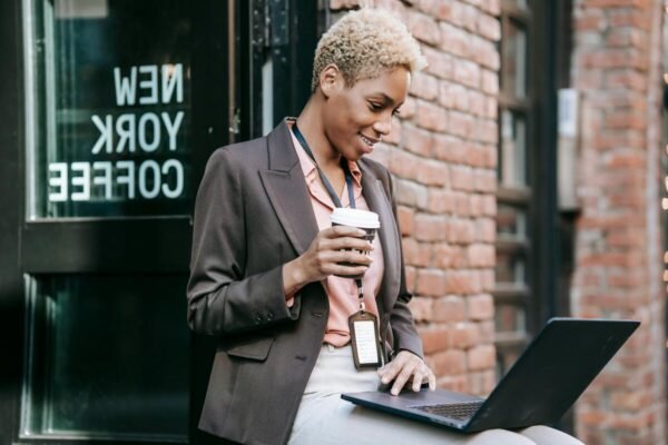 "Professional woman holding coffee while working on a laptop outside a coffee shop"