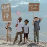 "Four diverse children standing on a beach holding eco-friendly signs for Earth conservation"