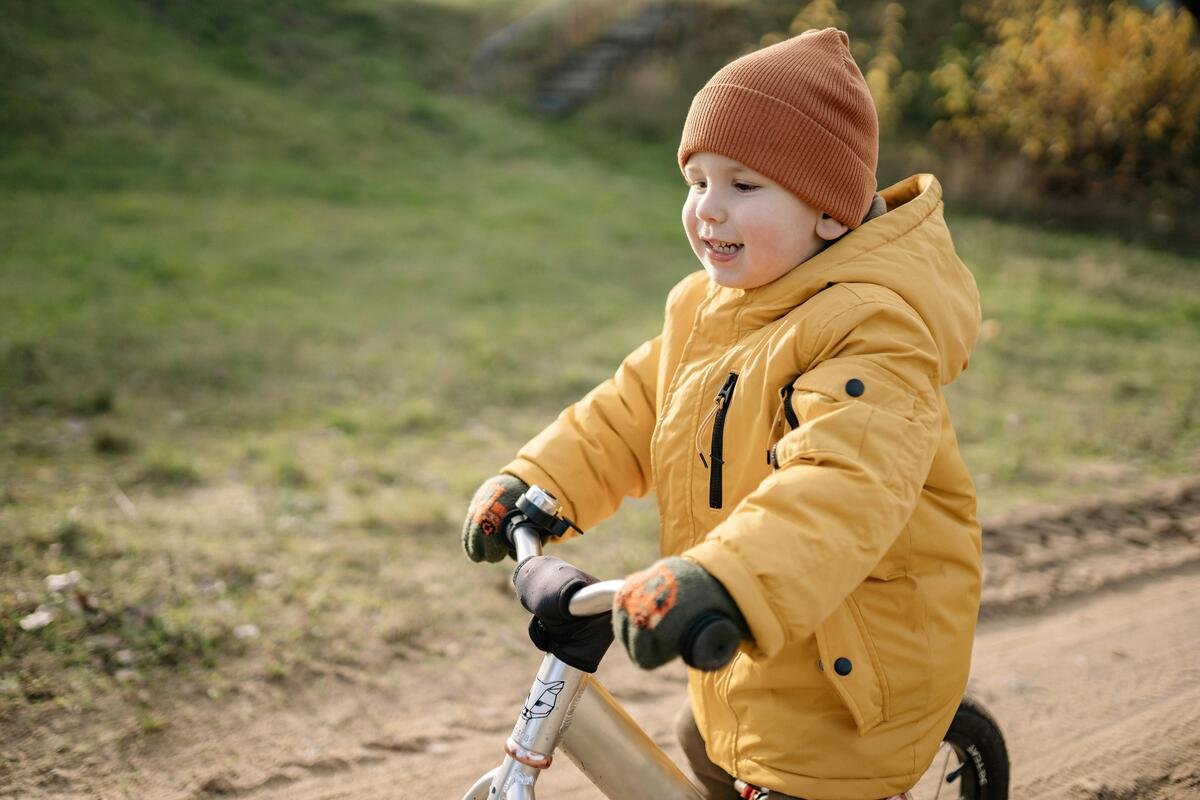 "Child in a yellow jacket riding a balance bike outdoors"