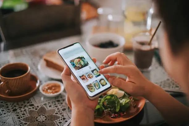 Person using a mobile app to browse food delivery options during a meal."