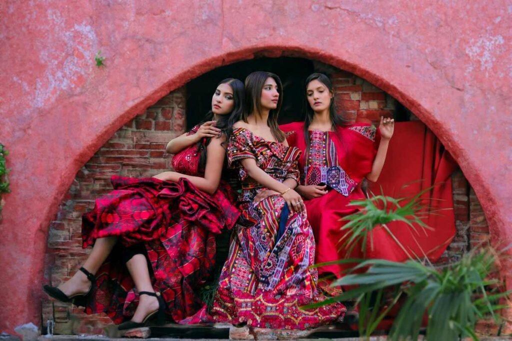 "Three women in vibrant traditional dresses seated in an arched rustic setting"