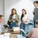 "Group of young students talking and studying together in a classroom with books and laptops"