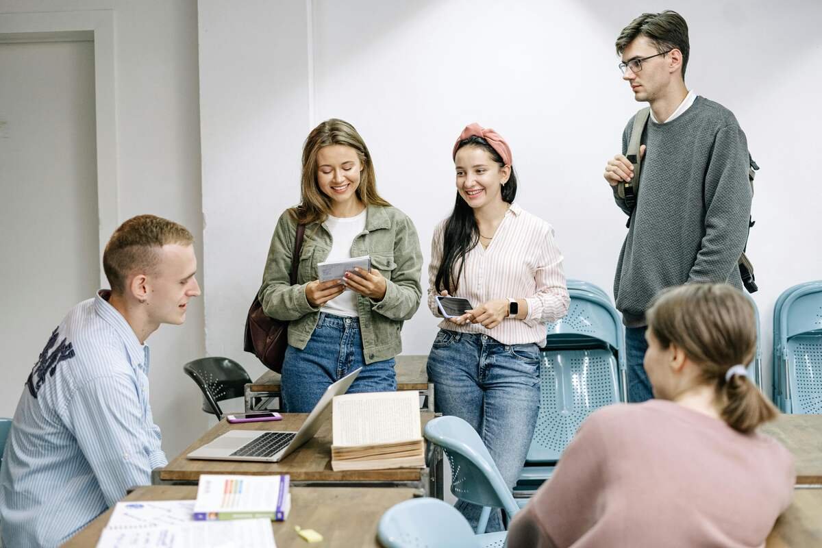 "Group of young students talking and studying together in a classroom with books and laptops"