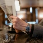 "Man in a gray suit reading a newspaper at a bar with a silver watch on his wrist"