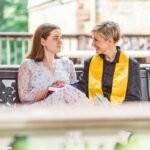 "Young woman holding a book and talking to a female minister in yellow stole on a bench"