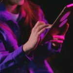 "Person interacting with a tablet in neon pink and purple lighting, wearing a purple shirt."