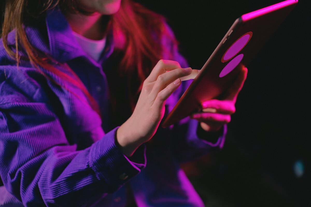 "Person interacting with a tablet in neon pink and purple lighting, wearing a purple shirt."