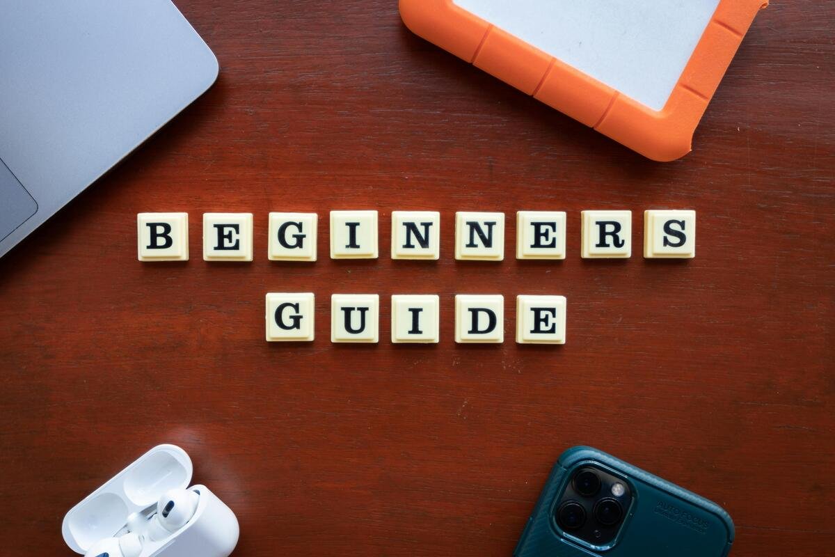 "Beginner's Guide spelled with tiles on a wooden table surrounded by gadgets and tech items"