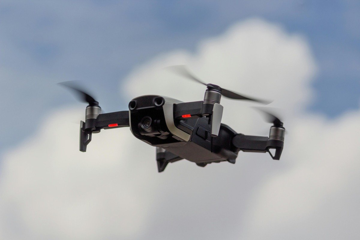 Black quadcopter drone flying against a blue sky with white clouds