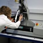 Scientist in a white lab coat operating an industrial testing machine in a laboratoryScientist in a white lab coat operating an industrial testing machine in a laboratory