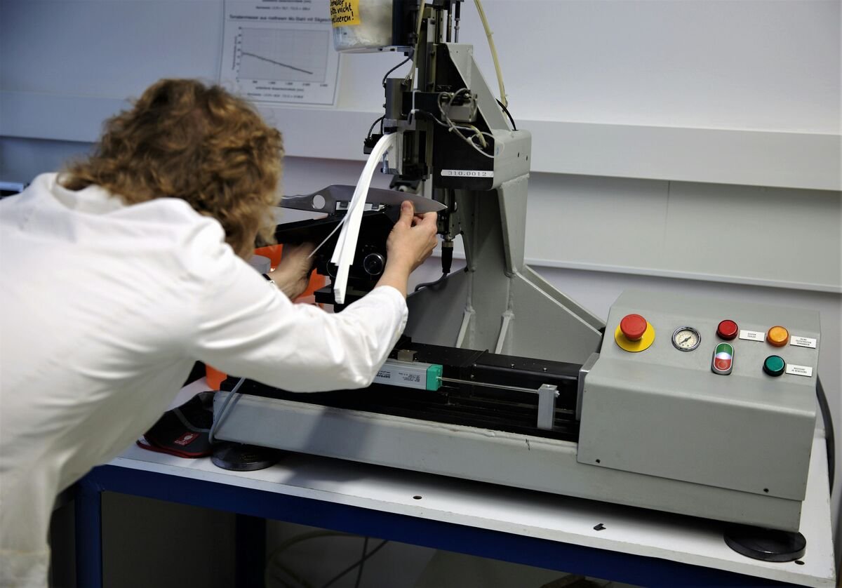 Scientist in a white lab coat operating an industrial testing machine in a laboratoryScientist in a white lab coat operating an industrial testing machine in a laboratory