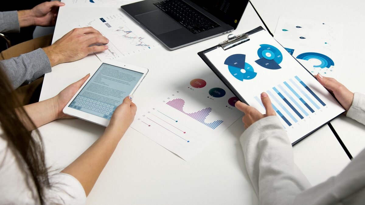 "Business professionals analyzing data charts and reports on a digital tablet and clipboard in a meeting.