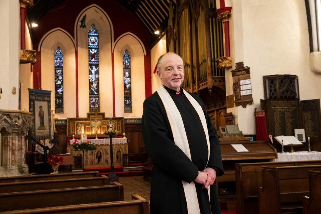 Reverend standing inside a church with stained glass windows and an altar in the background.